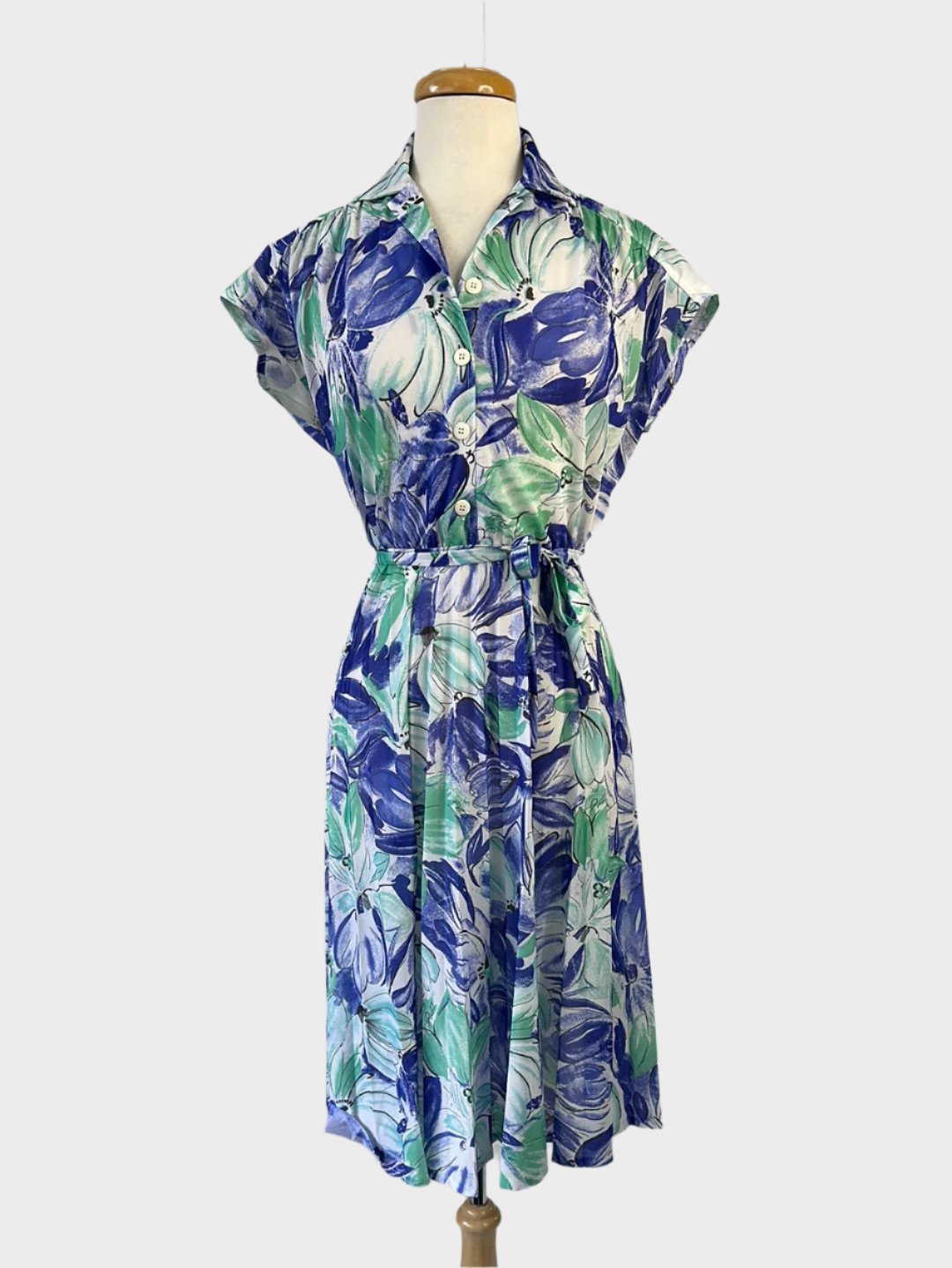 Vintage 60's A-line shirt dress in blue and green floral print with button-up front, notched collar, drop shoulders, waist sash, and pleated skirt for smart casual wear."