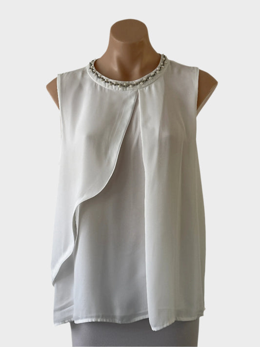 Liz Jordan sleeveless dress in white sheer crepe, featuring pleated front with draped overlay, round neck with diamante and pearl trim, yoke back, and shirt tail hem for special events or formal occasions.