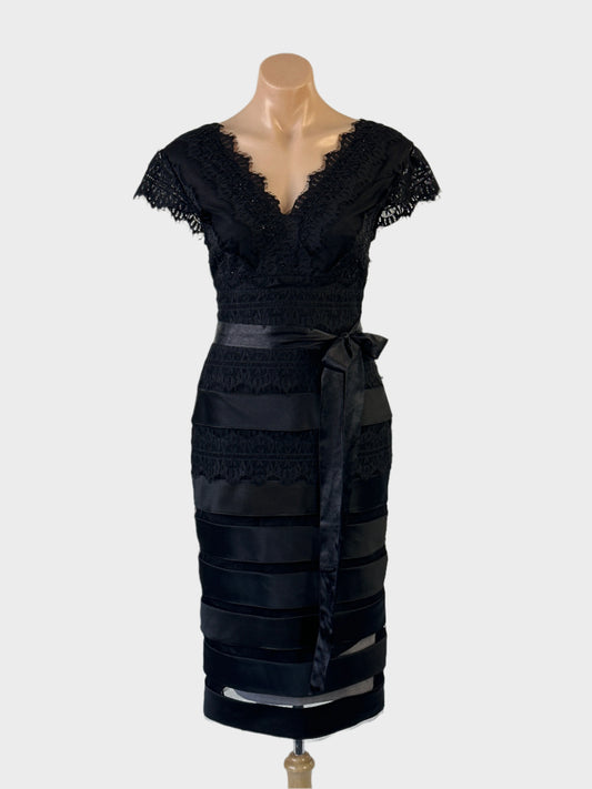 Designer Anthea Crawford sheath dress in black lace with scalloped edging, cap sleeves, v-shaped back, midriff yoke with satin sash tie and straight skirt with sheer mesh and satin tiers for evening or formal.