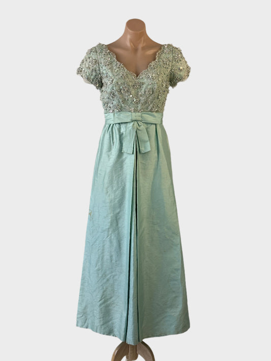 Vintage designer Jinoel of Melbourne gown in blue shantung with lace bodice, v-neck, decorative bow and pleated skirt for formal wear.