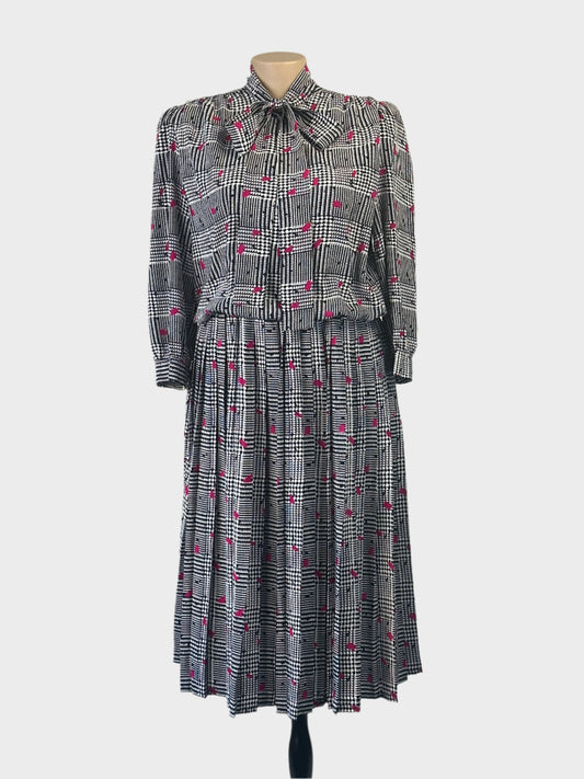 Vintage 80’s Noel Wells blouson dress in houndstooth check with contrasting flecks, band collar with pussy bow tie, and pleated skirt for office or special events.