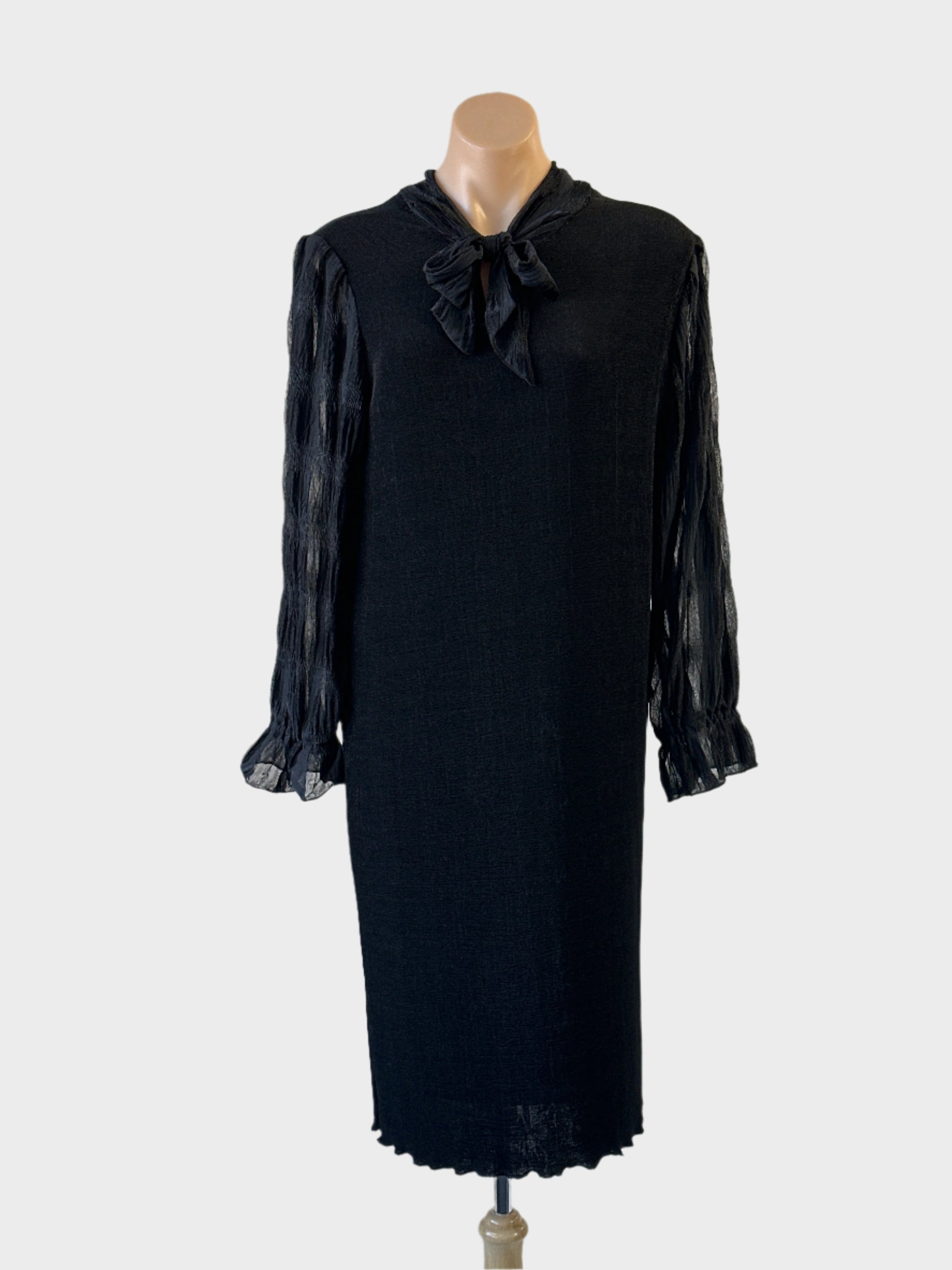 Shift dress in black knit with sheer sleeves and pussy bow neck for evening or formal wear.